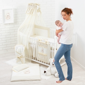 Jasno beżowa pościel z baldachimem na krótszym boku łóżeczka.